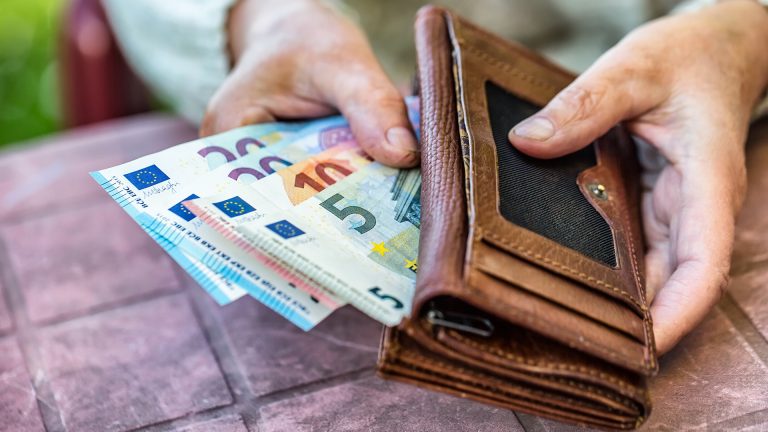 Das Pflegegeld steigt ab 2024: Auf dem Bild sind die Hände einer älteren Dame abgebildet, die eine braune Geldbörse halten, aus der mehrere Euroscheine ragen.