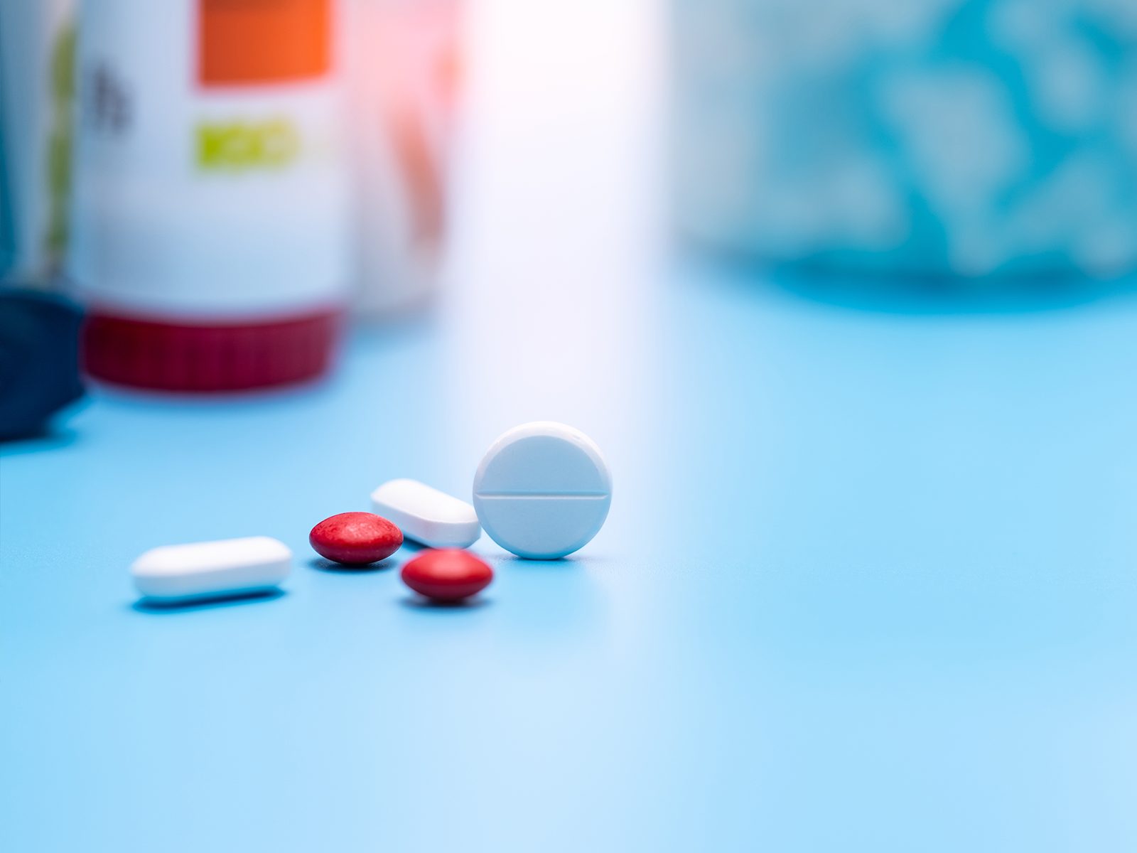 Selektiver Fokus auf runde weiße und rote Tabletten vor einer unscharfen Plastikflasche mit Medikamenten. Den Medikamentenplan einhalten: Das ist gar nicht so leicht bei mehreren Präparaten den.