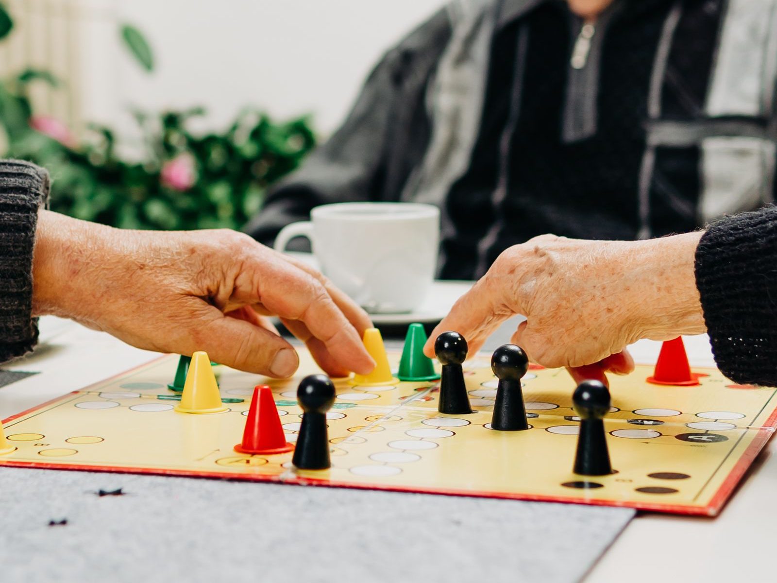 Nahaufnahme: Mehrere ältere Personen halten sich beim Spiel "Mensch ärgere dich nicht " geistig fit.