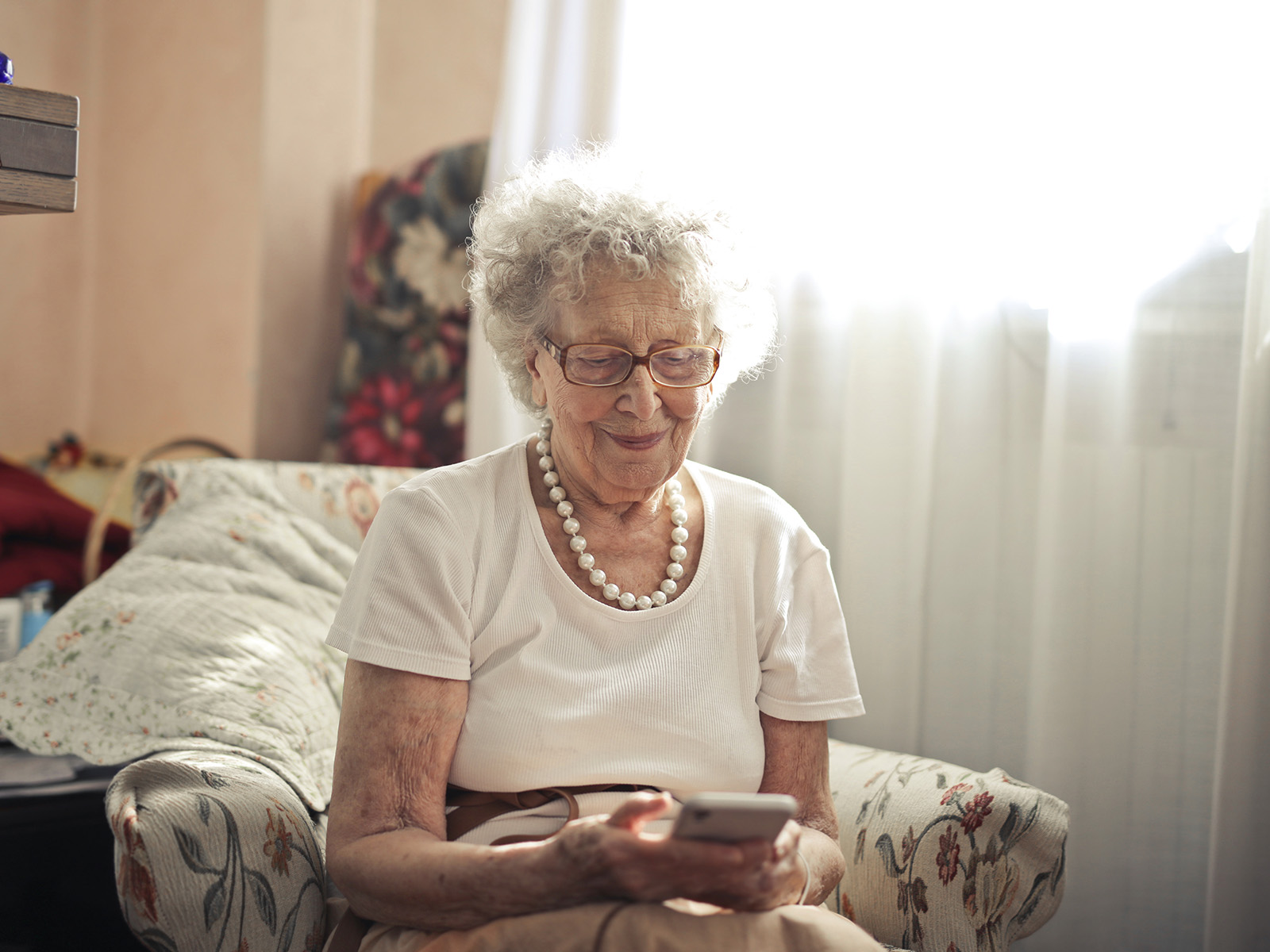 Eine Seniorin sitzt im Wohnzimmer und sieht lächelnd auf das Smartphone in ihren Händen. Digitale Gesundheitstools können insbesondere im Alter eine nützliche Hilfe sein.
