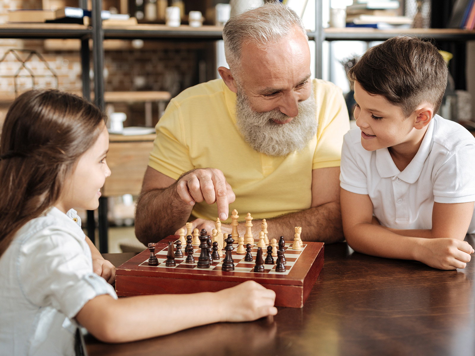 Gehirnjogging für Senioren: Ein älterer Mann spielt mit seinen beiden Enkelkindern Schach