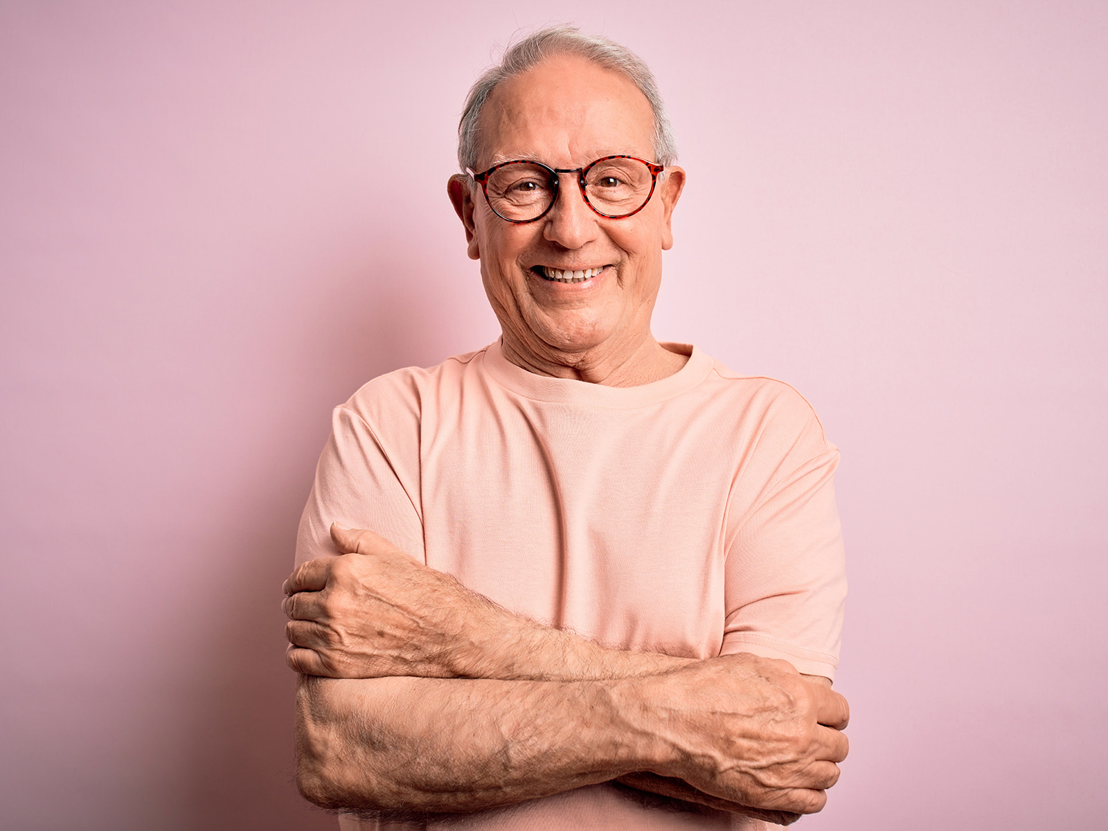Älterer Mann steht vor rosafabener Wand und lacht in die Kamera. Humor und Lachen sind wichtiger für uns als wir denken.
