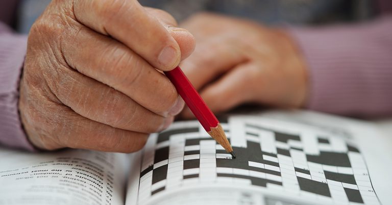 Eine ältere Person hält einen Stift in der Hand und löst ein Rätsel in einem Rätselblock