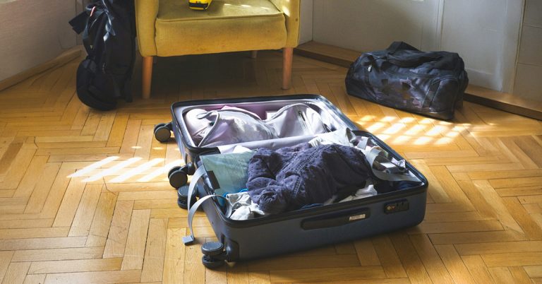offener, gefüllter Koffer in einer Altbauwohnung. Mit den richtigen Packtipps reisen Seniorinnen und Senioren unbeschwert.