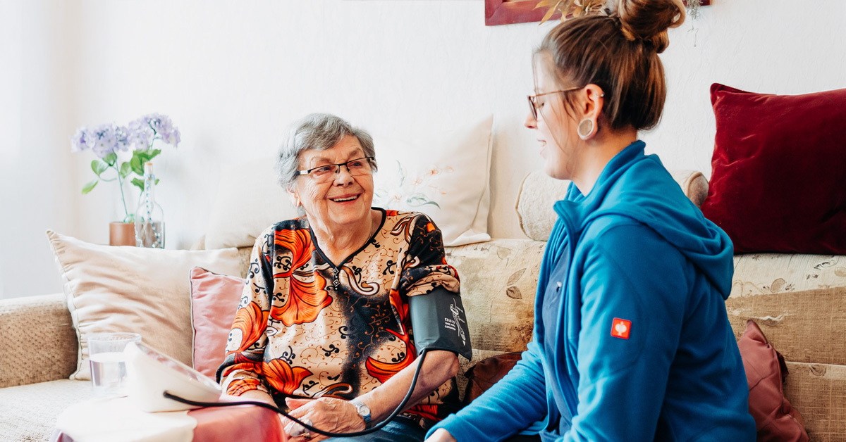 Eine Mitarbeiterin von Solitas misst bei einer Klientin Blutdruck. Diese Hausbesuche sind typisch für den Pflege-Beruf.