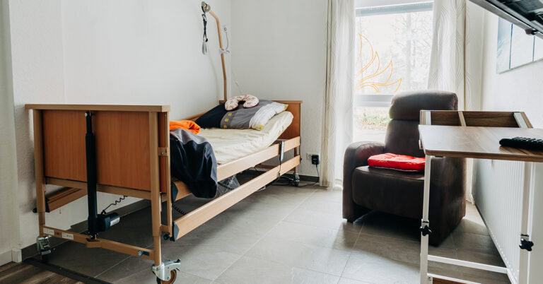 Ein Zimmer mit Pflegebett, Sessel und Tisch